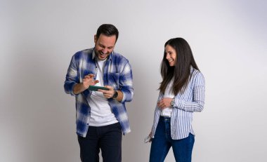 Akıllı telefondan video oyunu oynayan oyuncu sevgiliye bakan gülümseyen genç kız arkadaş. Cep telefonlu neşeli bir çift arka planda durup poz veriyor.
