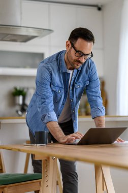 Gözlüklü odaklanmış genç işadamı rahat ofis masasında dizüstü bilgisayarla çalışmaya odaklanmış.