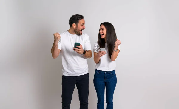 若いカップルは スマートフォンで商品ニュースを受け取った後 拳をポンピングし 興奮して叫んでいます 背景にテキストメッセージを読んだ後 幸せそうにお互いを見て恍惚と男と女 — ストック写真