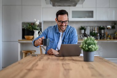 Gülümseyen genç işadamı elinde kahve fincanı ve video ile ofisteki masadan arıyor.