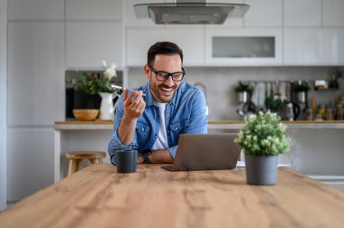 Neşeli iş adamı, ev ofisinde gözlük takan müşterisiyle hoparlörden konuşuyor.