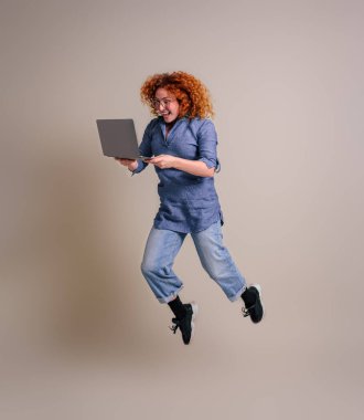 Neşeli kadın profesyonel dizüstü bilgisayar tutuyor ve arka planda kendinden geçmiş bir şekilde zıplıyor.