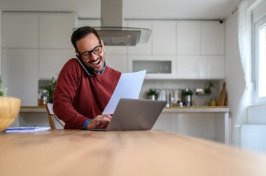 Neşeli genç girişimci telefon görüşmesinde belgeyi tartışıyor ve ofisteki bilgisayarı kullanıyor.