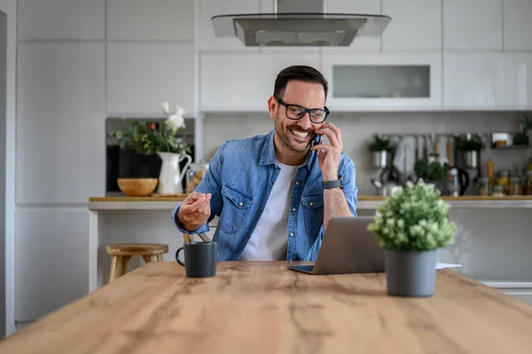 stock image Male entrepreneur smiling and communicating over mobile phone with laptop on desk in home office