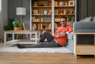 Ofisteki kanepe başında otururken cep telefonuyla neşeli iş adamı mesajlaşması.