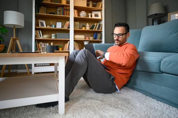 İş adamı kol saatini kontrol ediyor ve ofisteki kanepede otururken dizüstü bilgisayarla çalışıyor.