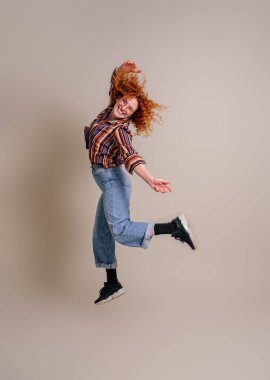 Neşeli, heyecanlı, kızıl saçlı genç bir kadın arka planda izole bir şekilde havaya atlıyor.