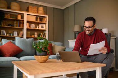 Elinde hesap tabloları olan mutlu bir erkek mali danışman ve merkez ofisteki laptop üzerinden analiz raporları.