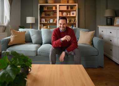 Gözlüklü ve oturma odasındaki kanepede oturan gülümseyen yakışıklı girişimcinin portresi.