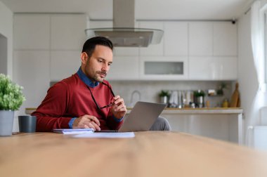 Ofisteki bilgisayarı kullanırken elinde gözlük tutan ve düşünen yakışıklı girişimci.