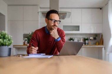 Ciddi bir erkek serbest yazar evdeki kablosuz bilgisayardan araştırma yaparken notlar yazar.