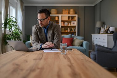 Zarif takım elbiseli genç bir erkek ofis masasında dizüstü bilgisayarla araştırma yapıyor.