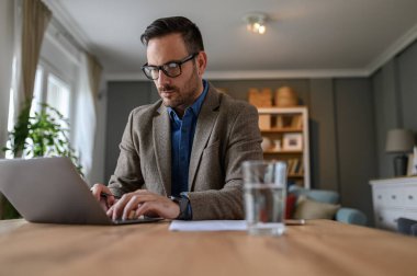 Seçkin takım elbiseli bir yöneticinin düşük açılı görüntüsü evdeki masada dizüstü bilgisayarla çalışıyor.