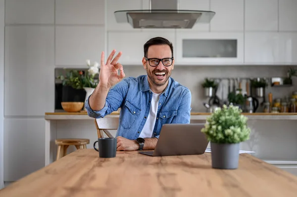 stock image Portrait of successful businessman showing OK sign while working over laptop on desk at home