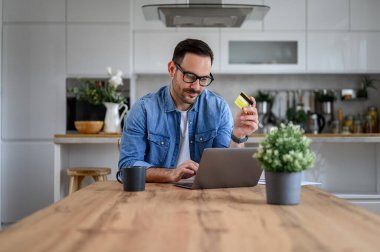 Yakışıklı iş adamı bilgisayarında kredi kartıyla internetten alışveriş yapıyor.