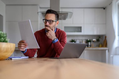İşletme raporunu analiz eden odaklanmış erkek girişimci ve ofis masasında dizüstü bilgisayarla çalışıyor.