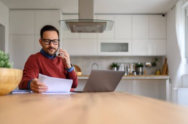 Ciddi bir iş adamı, iş yerinde çalışırken telefon üzerinden mali belgeleri tartışıyor.