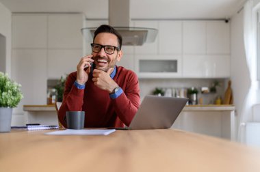 Ofiste masa başında otururken cep telefonuyla konuşan eli çenesinde yakışıklı bir genç.