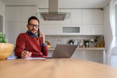 Genç işadamı, ofis telefonunda iş görüşmelerini tartışırken fikirler yazıyor.