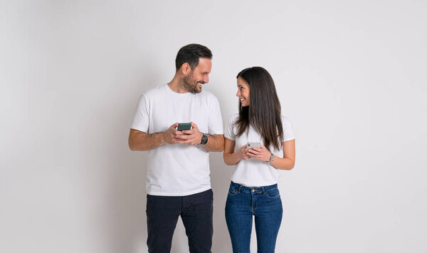 Romantic young couple with mobile phones smiling and looking at each other against white background