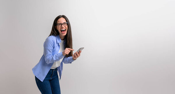 Cheerful female entrepreneur in glasses laughing at camera while using cellphone on white background