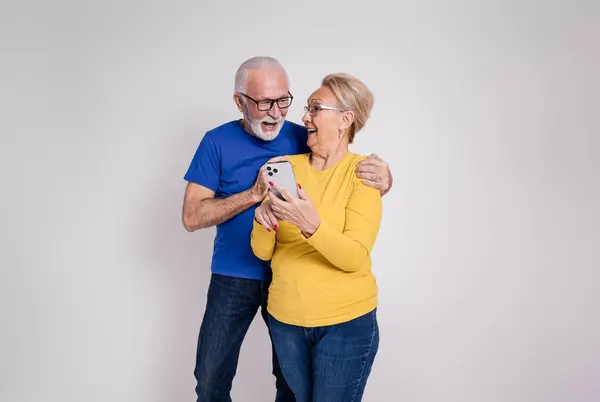 Happy senior couple screaming and looking at each other after reading good news on white background