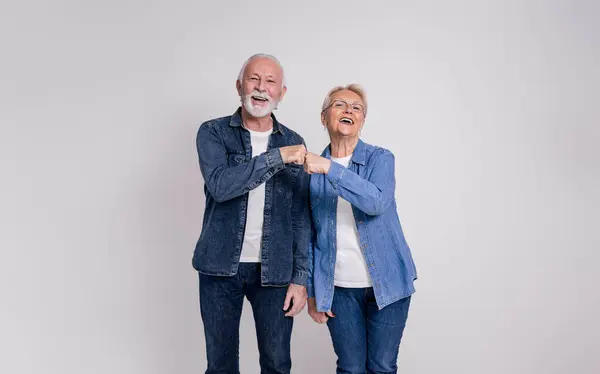 Portrait of happy senior couple laughing and giving fist bumps while standing on white background