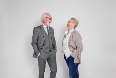 Elleri ceplerinde birbirine bakıp beyaz arka planda gülen mutlu kıdemli meslektaşlar.