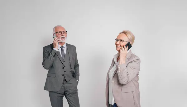 Smiling elderly businessman and businesswoman discussing over smart phones against white background
