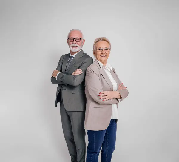 Confident senior partners with arms crossed smiling and posing back to back on white background