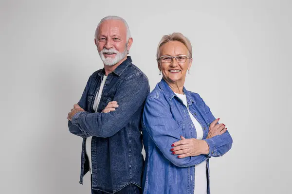 Portrait of smiling old husband and wife with arms crossed standing back to back on white background