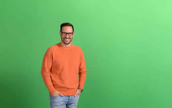 Stock image Portrait of successful handsome freelancer with hands in pockets smiling against green background