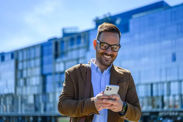 Smiling Businessman Texting Smart Phone While Standing Modern Office Building Ліцензійні Стокові Зображення