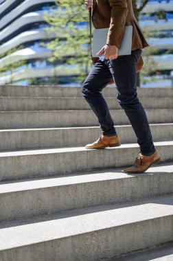 Erkek profesyonelin dizüstü bilgisayarı tuttuğu ve güneşli bir günde şehrin merdivenlerine tırmandığı bölüm.