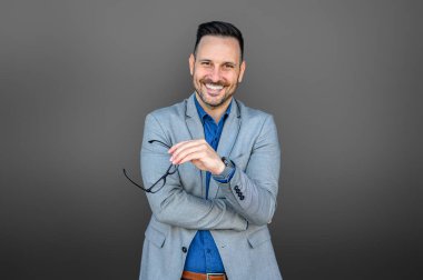 Gözlük tutan başarılı iş adamının portresi ve gri arka planda çapraz kol pozu.