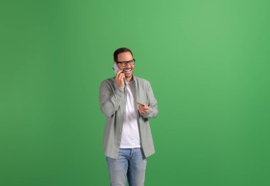 Kredi kartı ile neşeli genç adam cep telefonundan konuşuyor ve yeşil arka planda duruyor.