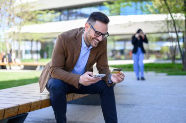 Akıllı telefon ve kredi kartıyla internet üzerinden ödeme yapan mutlu bir erkek.