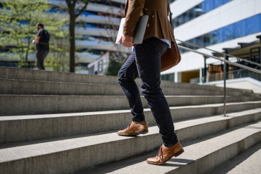 Modern şehirde merdivenlerde yürüyen omuz çantası ve dizüstü bilgisayarı olan düşük seviyeli bir adam.