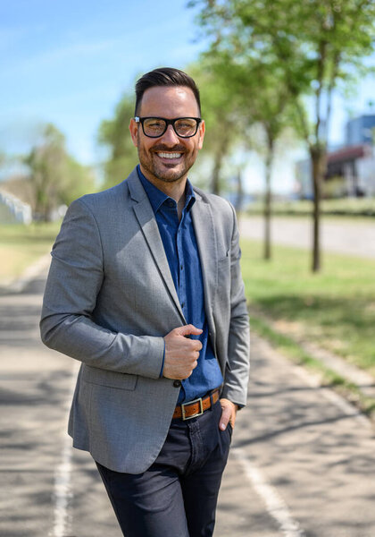 Portrait of confident male entrepreneur in eyeglasses posing happily on street in modern city