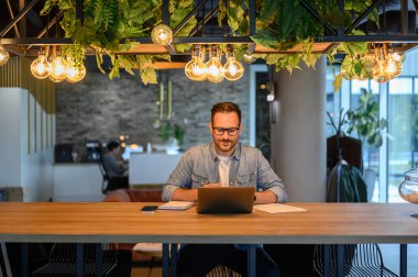 Aydınlanmış ofiste masa başında otururken dizüstü bilgisayar üzerinde çalışan kendinden emin erkek programcı