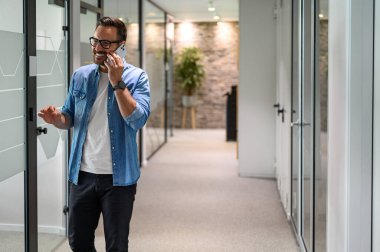 Ofis koridorunda yürürken proje detaylarını telefonda tartışan yakışıklı girişimci