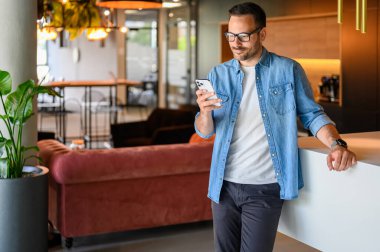Modern ofiste cep telefonundan internet mesajlarını kontrol eden gözlüklü yakışıklı bir finans danışmanı.