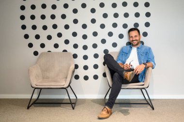 Modern ofiste rahat rahat oturan, gözlüklü, kendinden emin bir iş adamı.