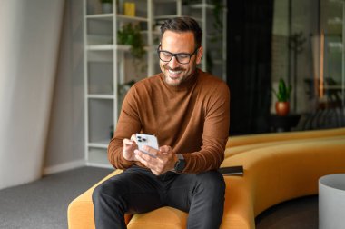 Ofiste otururken cep telefonundan gülümseyen ve mesajları okuyan yakışıklı işadamının portresi