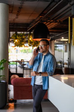 Gözlüklü mutlu mühendis ofiste beklerken müşteriyle telefonda konuşuyor.