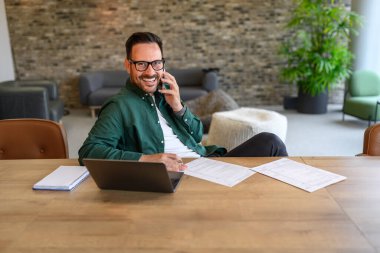 İş yerinde gülümseyen ve cep telefonuyla konuşan kendine güvenen bir iş adamının portresi.