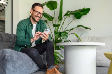 Modern ofisteki koltukta otururken cep telefonuyla uygulamaları kullanarak tam boy serbest çalışan