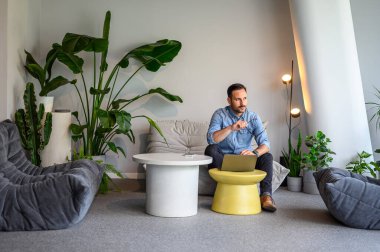 Ofisteki kanepede dizüstü bilgisayarla otururken gözlüklü bir girişimci gözlerini kaçırıyor.