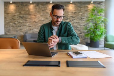 Ofisteki bilgisayarın başında çalışırken erkek proje yöneticisi kol saatini kontrol ediyor