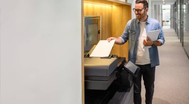 Kendine güvenen erkek girişimcinin portresi modern işyerindeki fotokopi makinesine boş kağıtlar koyuyor.